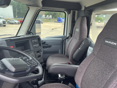 Truck cab interior showing driver and passenger seats with Mack branding, dashboard controls, steering wheel, and side windows.