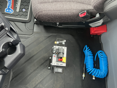 Tractor truck cab interior showing floor with gear selector and blue air hose, passenger seat, and rubber floor mat.