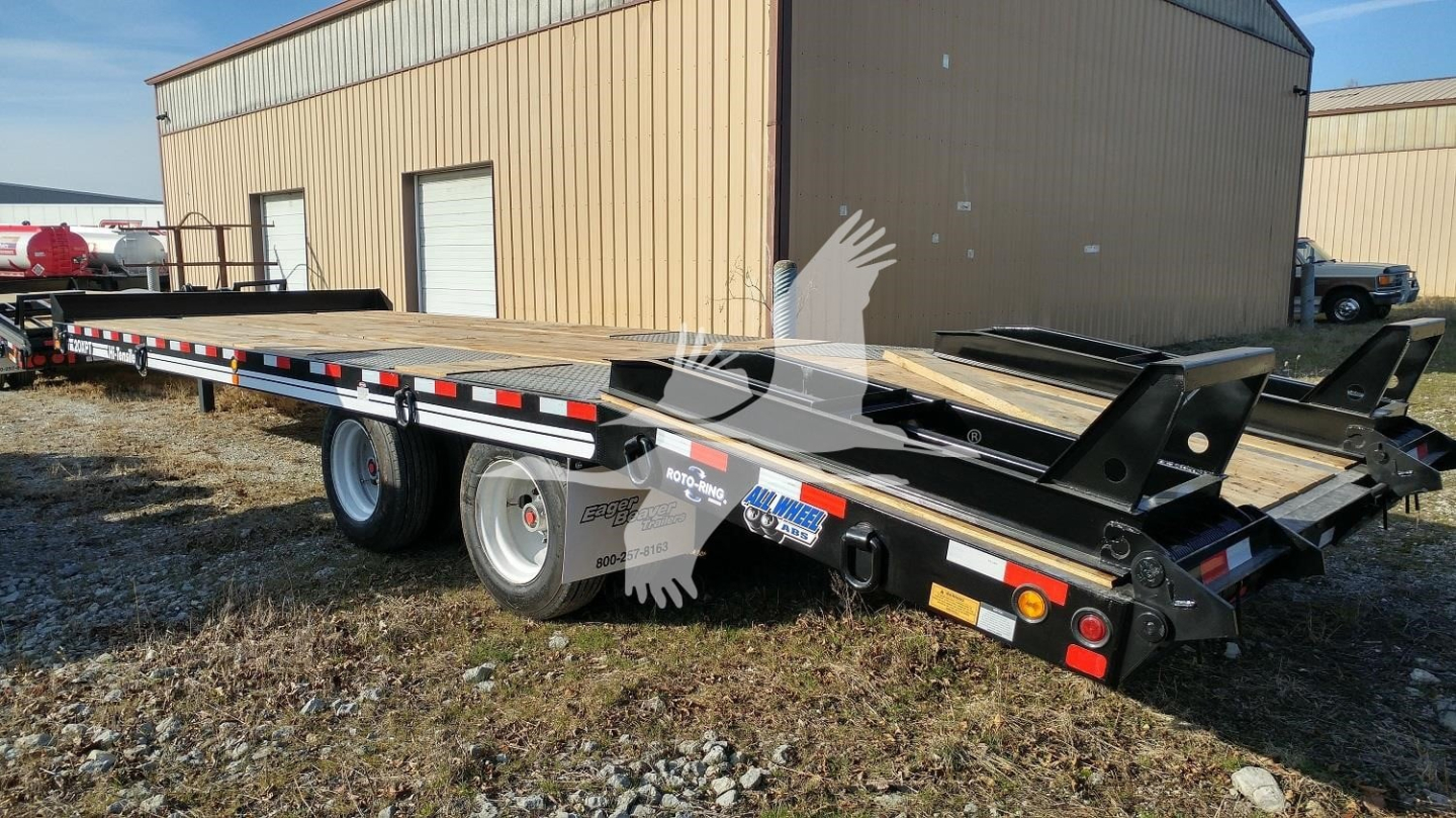 Trailer showing flatbed equipment and dual rear axles with black frame, red/white reflective tape, and ramp rear; brand stickers visible on side.