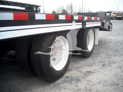 Trailer wheel assembly showing dual rear tires, white rims, and side rail with reflective tape on a flatbed trailer.