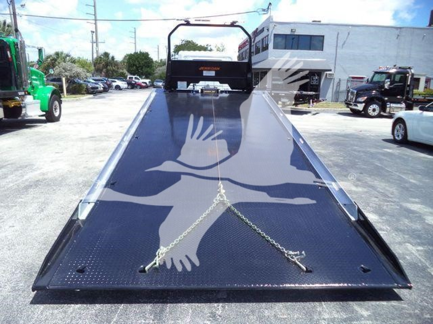 Flatbed tow truck bed on a 2026 Hino L6 rollback truck showing metal diamond-plate surface and safety chains.