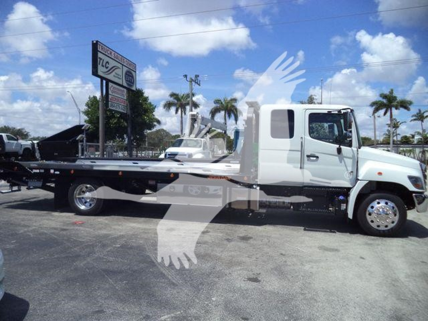 Flatbed tow truck side view showing cab and long flatbed with chrome wheels and parked in lot.