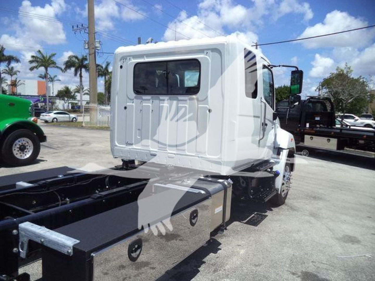 Truck cab side and rear view showing white 2026 Hino L6 rollback truck chassis, side rails, and rear cargo area with back window, parked at dealership lot.