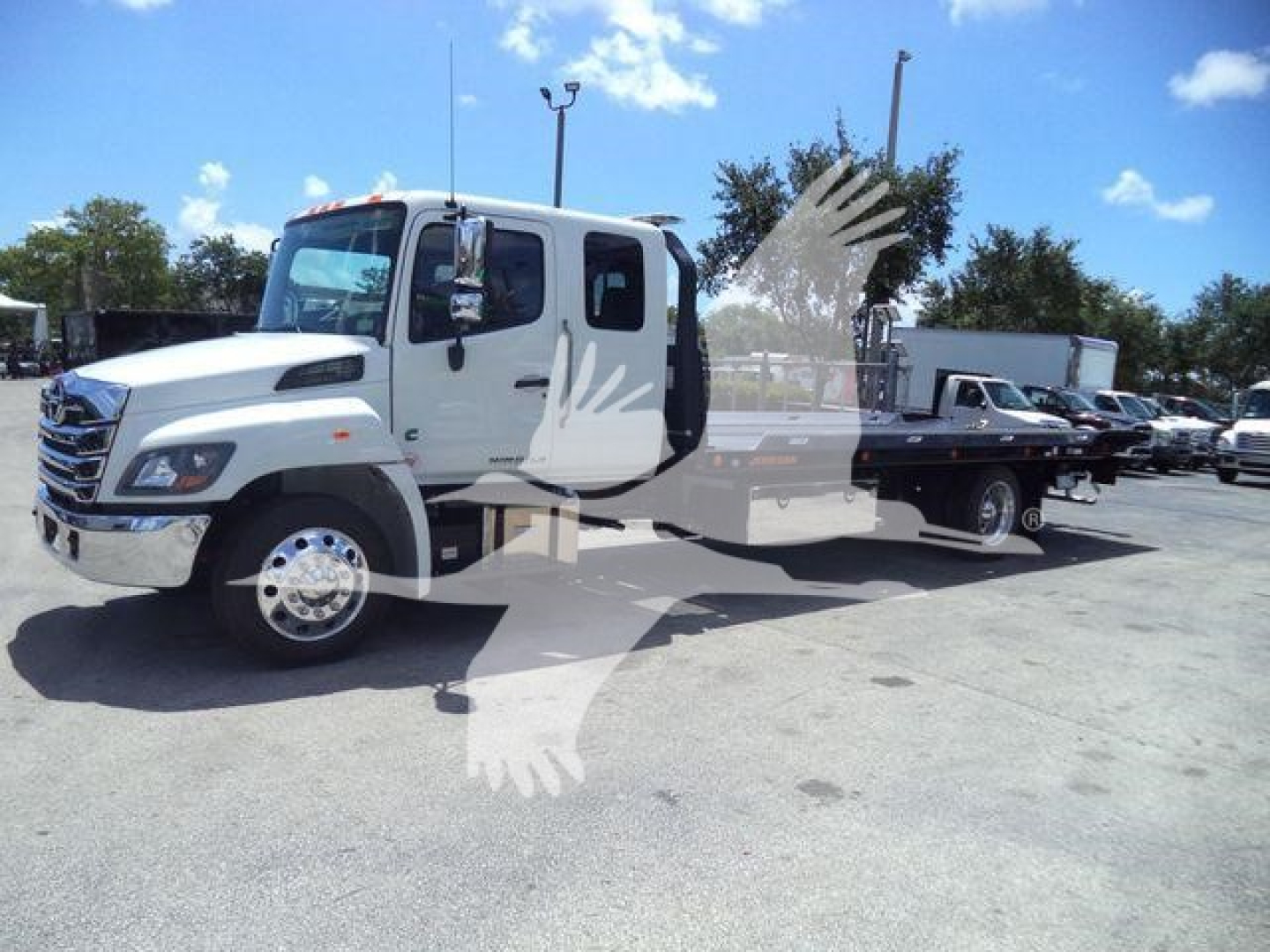 Truck cab and rollback wrecker body on a white Hino L6 chassis, side view, in a dealership lot.