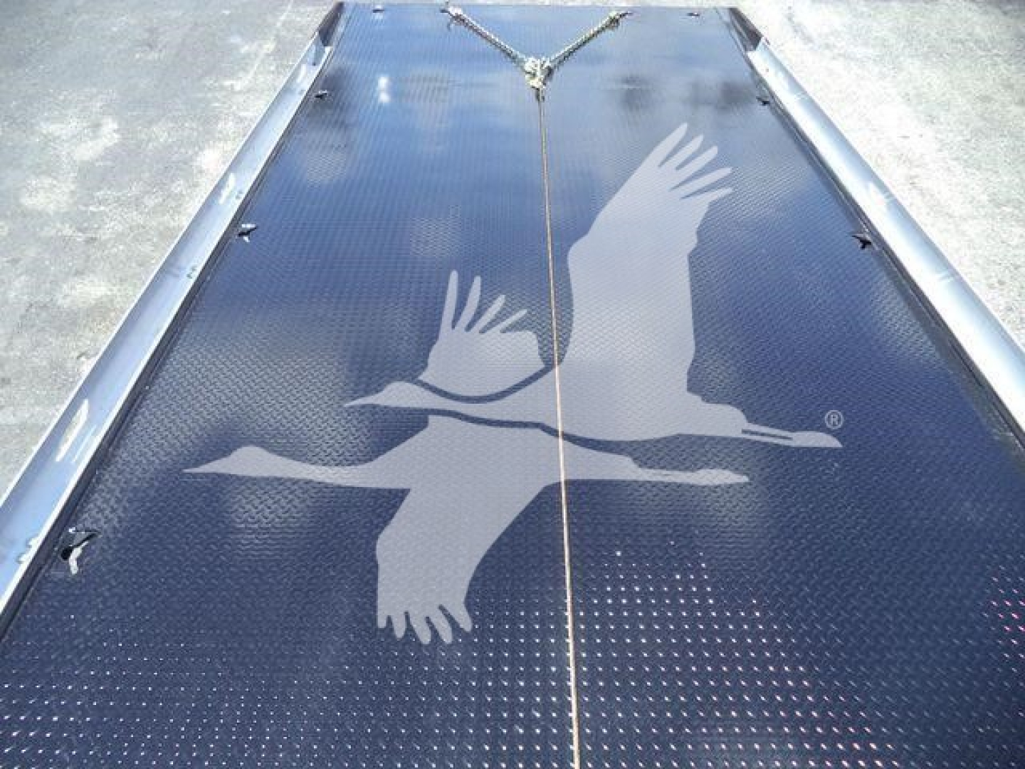 Flatbed trailer top with decorative gulls logo and tie-down strap, showing a textured black surface.