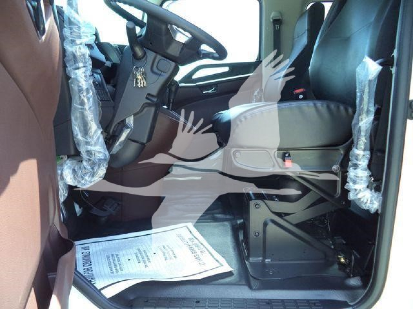 Truck cab interior view of a new Hino L6 with plastic-wrapped seats and steering wheel, showing driver's seat and dashboard area.