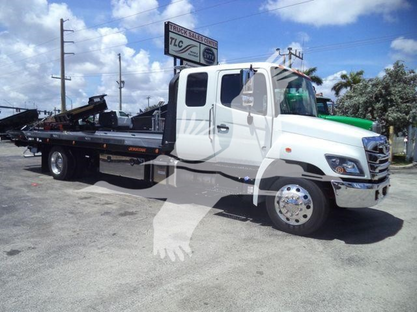 2016-? Hino L6 rollback truck with flatbed, white cab, green accents, side view showing wheel, mirror, and hydraulic equipment on bed.