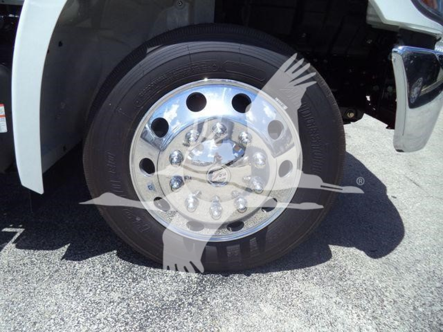 Wheel and tire close-up on a Hino truck front, chrome hubcap with multiple bolts and tire tread visible.