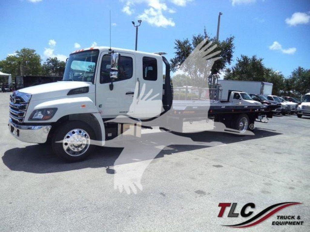 White Hino L6 rollback truck shown from front-left; overlay watermark of a bird and TLG Truck & Equipment logo; no visible text on vehicle parts.