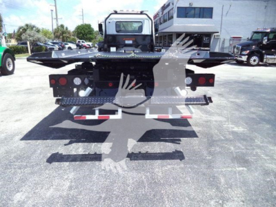 Back view of a new 2026 Hino L6 rollback tow truck chassis with flatbed and rear lighting, seen in a dealership lot.