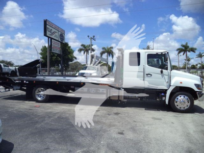 Flatbed tow truck side view showing cab and long flatbed with chrome wheels and parked in lot.