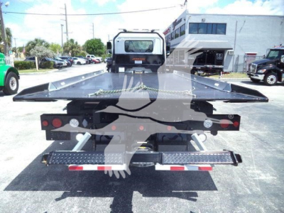 Front view of a new 2026 Hino L6 rollback tow truck showing a flatbed bed and rear equipment with dual hydraulic stow supports.