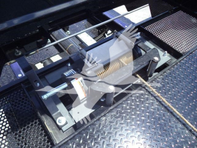 Trucks component view showing a winch or hoist mechanism with a coil spring, rollers, and steel framework on a diamond plate surface.