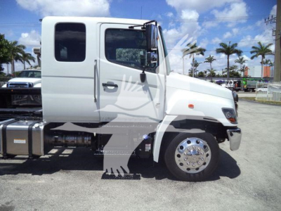 Truck cab side view showing white 2026 Hino L6 Rollback truck with large front wheel, side mirror, and dual exhaust area.