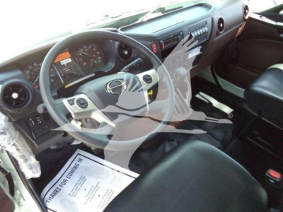 Dashboard and steering wheel of a 2026 Hino L6 truck interior with a wrapped steering wheel emblem, center console, and driver’s seat; visible instrument cluster and pedals.