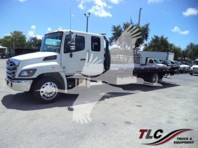 White Hino L6 rollback truck shown from front-left; overlay watermark of a bird and TLG Truck & Equipment logo; no visible text on vehicle parts.