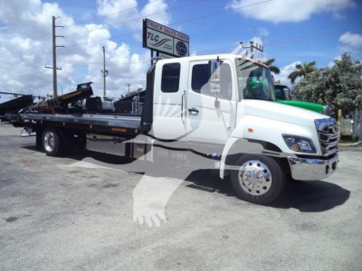 2016-? Hino L6 rollback truck with flatbed, white cab, green accents, side view showing wheel, mirror, and hydraulic equipment on bed.