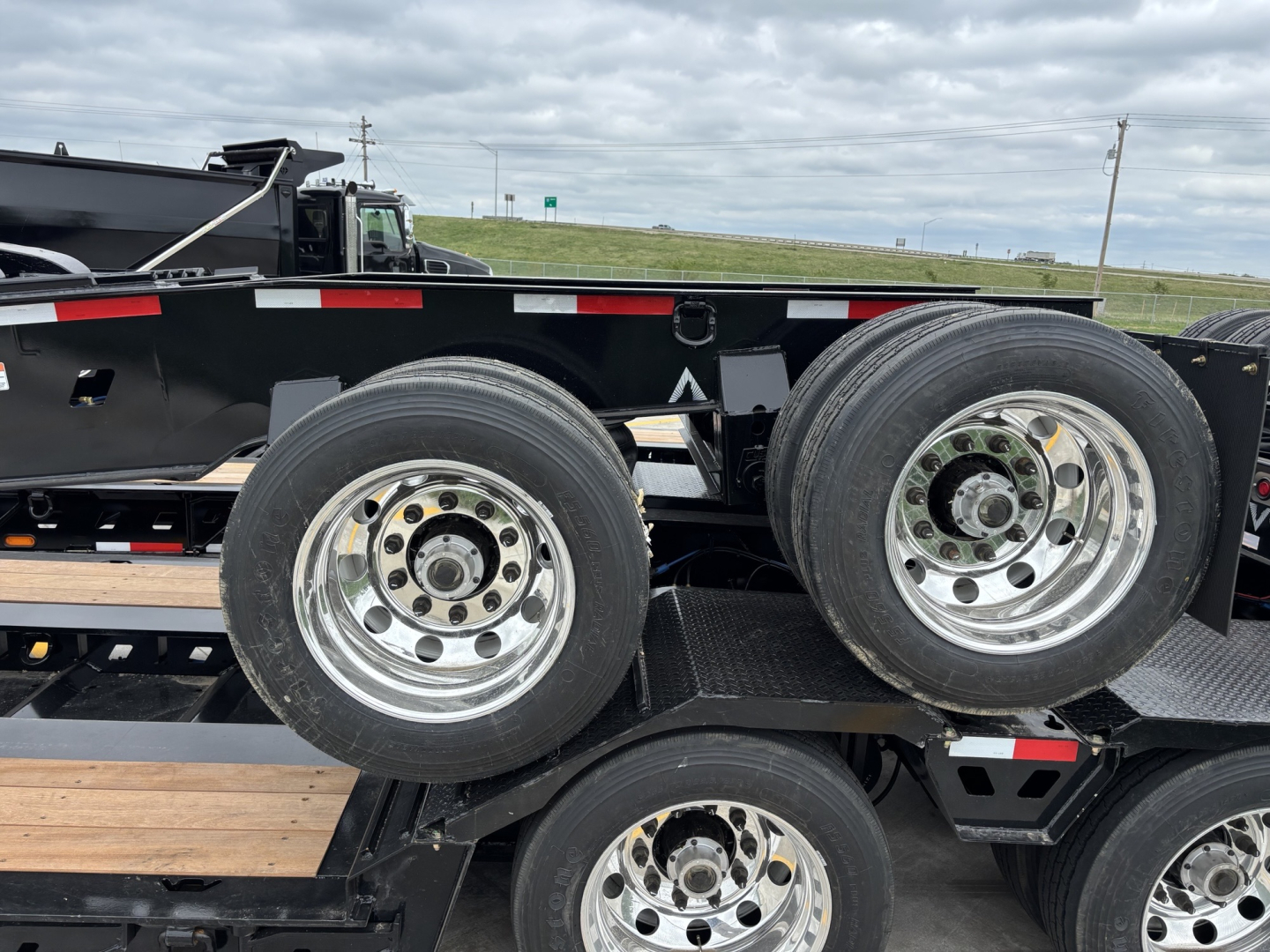 Trailer dolly showing dual rear axles with chrome wheels and black frame, tires visible on a flatbed trailer.