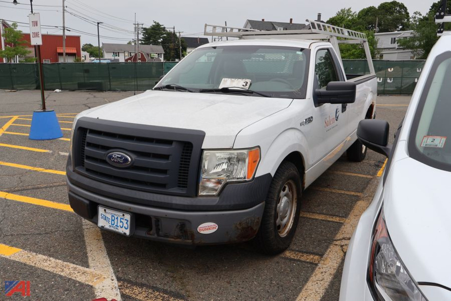 Ford F-150 pickup truck with utility bed and ladder rack, front bumper with stickers, license plate visible, in a parking lot.