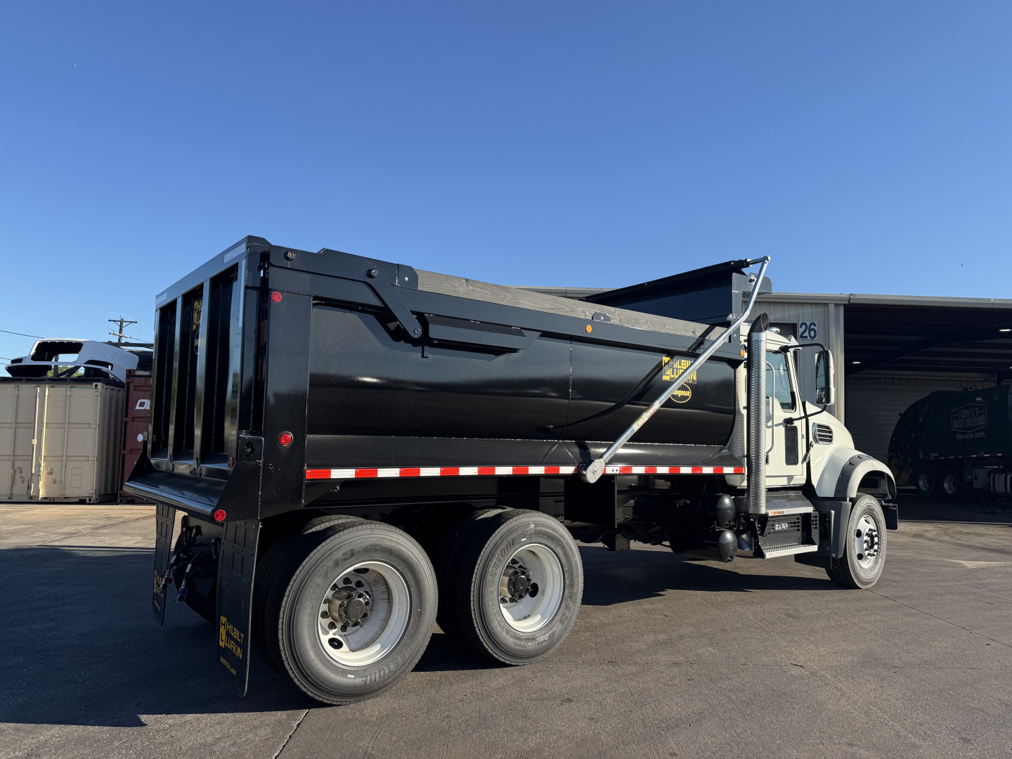 Dump truck showing a 2026 Mack GR64F dump body with black bed and white cab, side view, dual rear axles, VIN 1M2GR2GCXTM053541 visible in listing context.