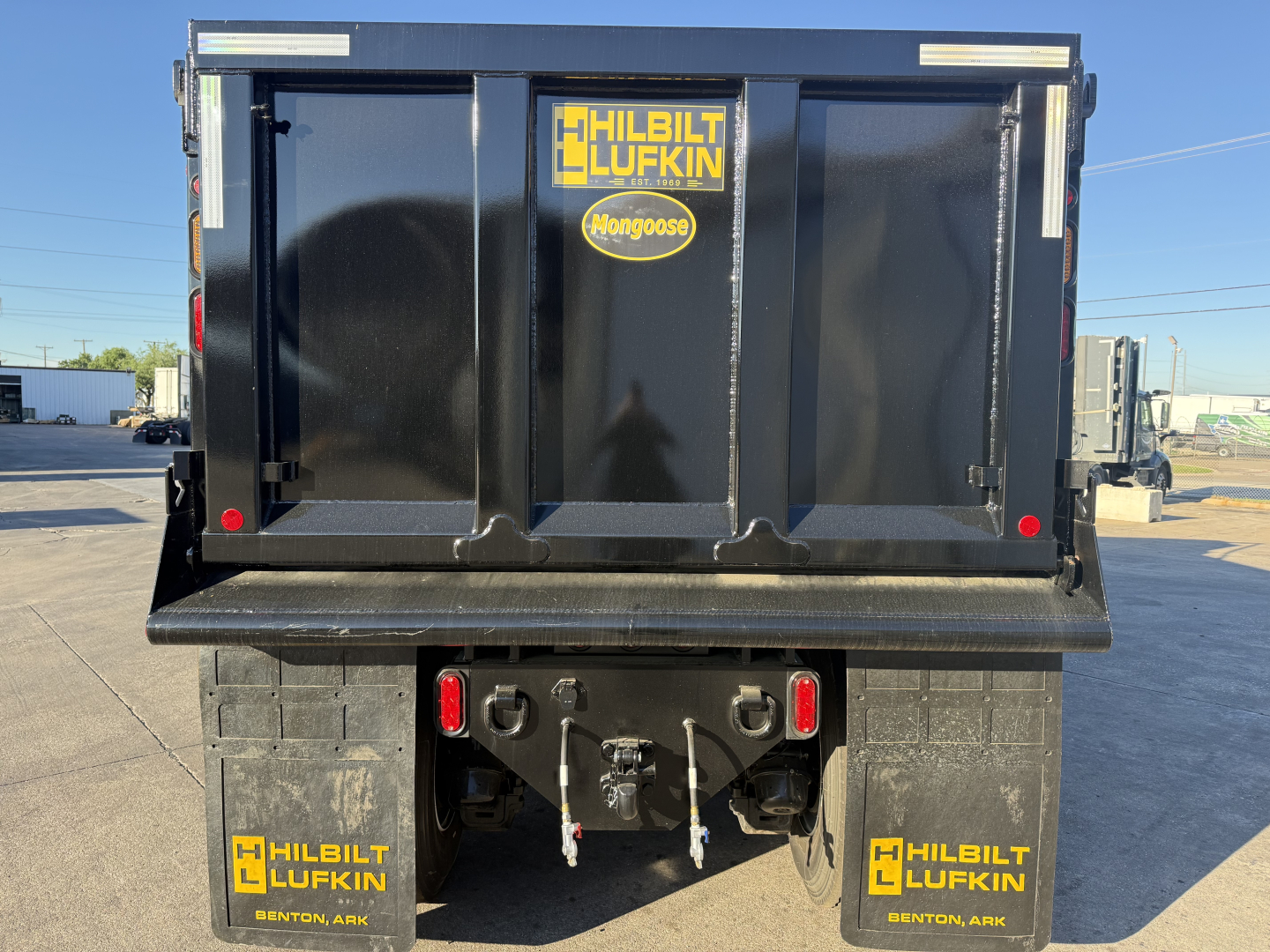 Dump truck bed showing rear with stickers reading HILBILT LUFKIN Mongoose on tailgate and side decals; view includes hitch and rear lights.
