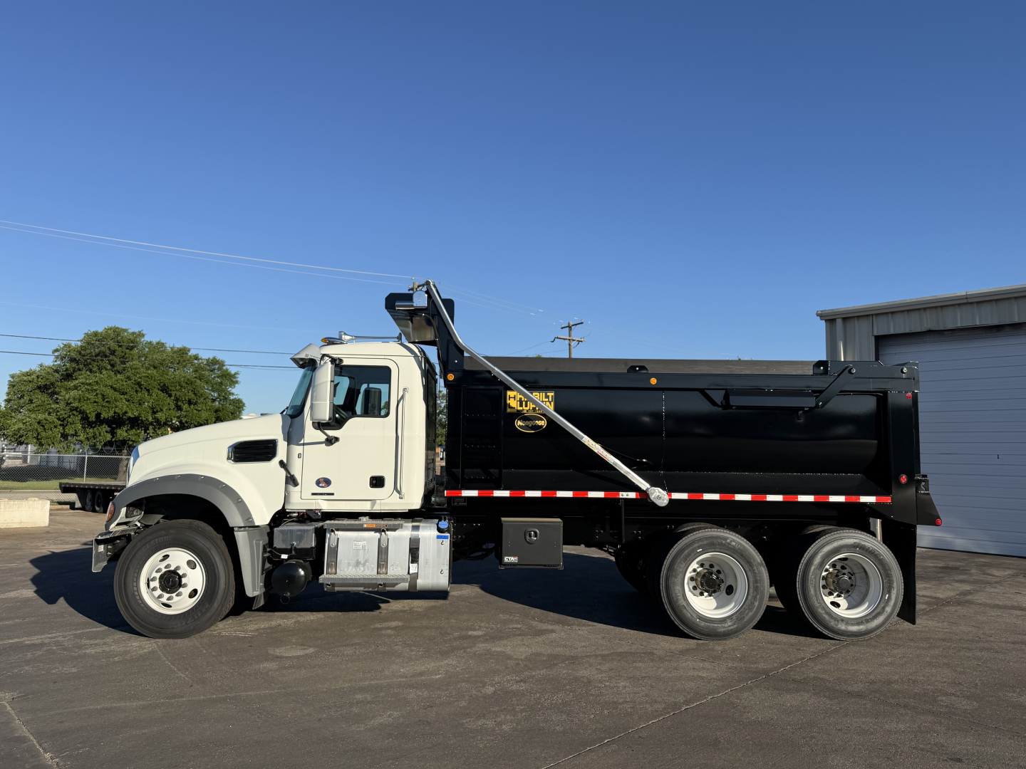 Truck side view of a 2026 Mack GR64F dump truck showing black dump body and white cab, with ladder and safety rails visible.
