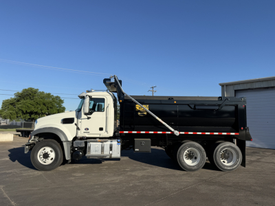Truck side view of a 2026 Mack GR64F dump truck showing black dump body and white cab, with ladder and safety rails visible.