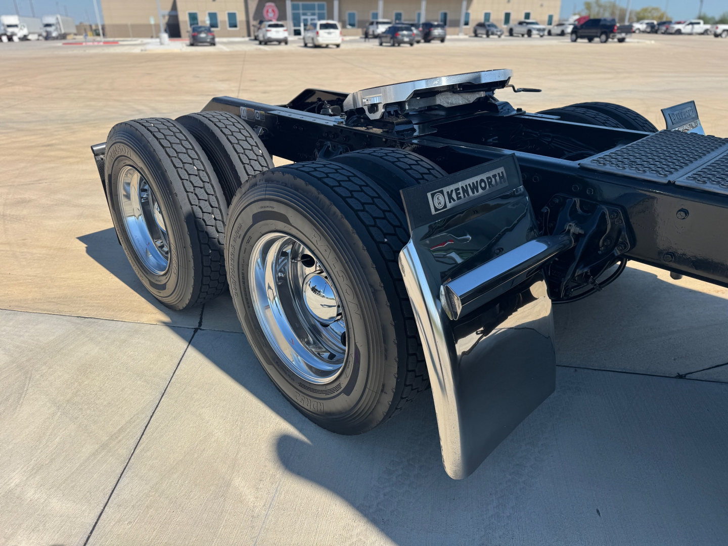 Kenworth W900L chassis rear view showing dual rear axles, mud flaps, chrome wheels, and fuel/air lines.