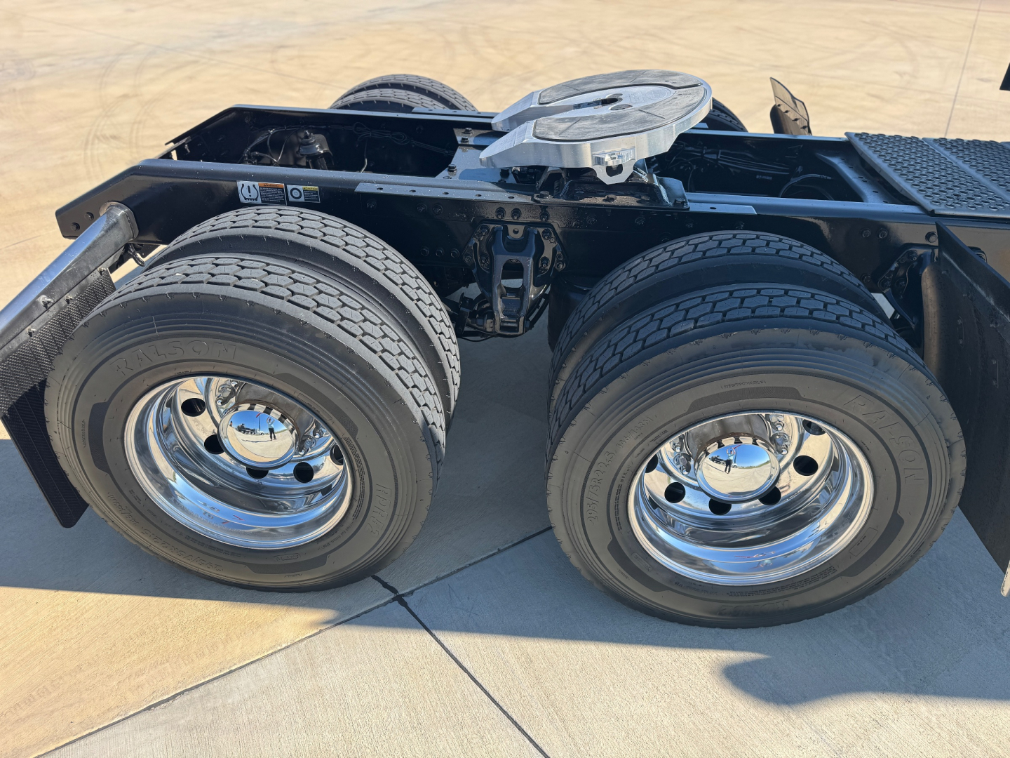 Kenworth W900L chassis showing dual rear axles and wheels with chrome rims, view of frame and fifth wheel in foreground.