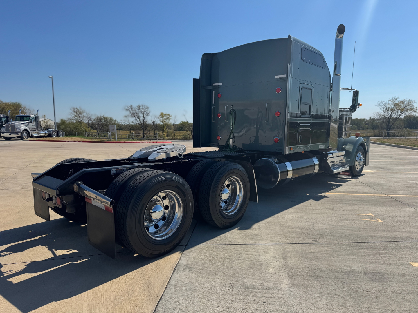 Kenworth W900L sleeper cab tractor (rear/side view) showing dual rear axles, black exterior, chrome fuel tanks, and exhaust stack.