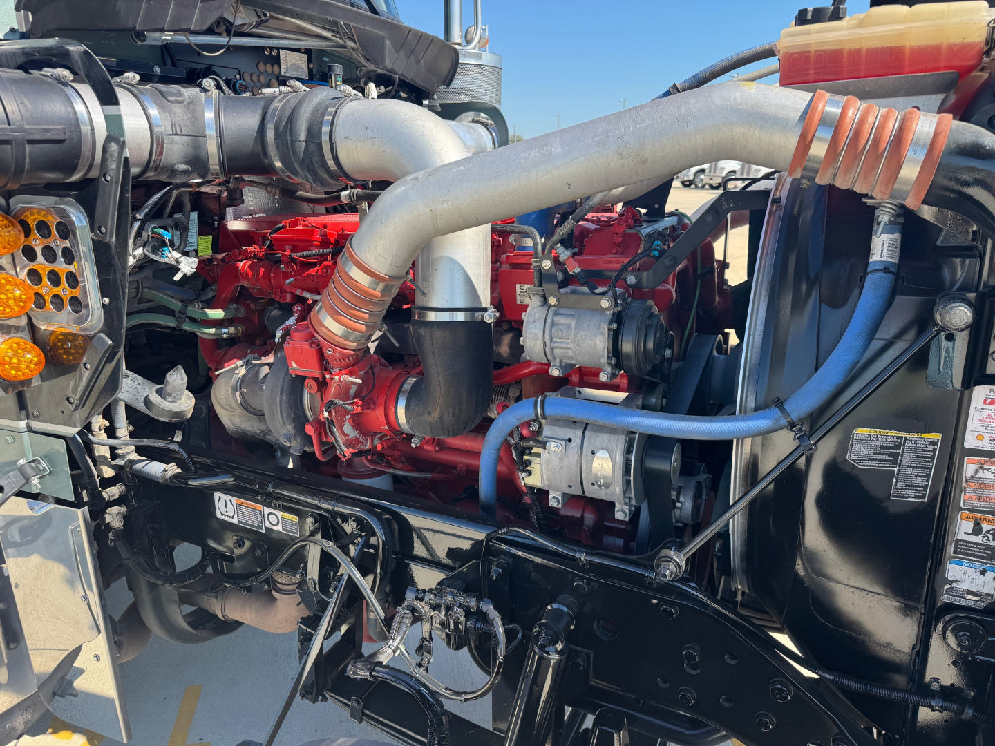 Kenworth W900L engine bay showing large turbo, red engine block, and various hoses and metal components.