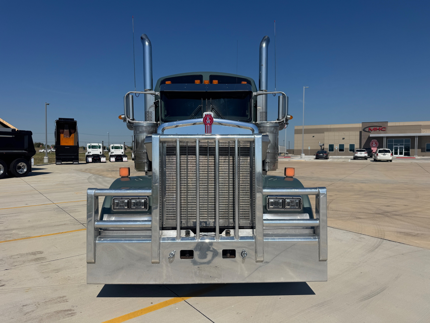 Kenworth W900L front view showing large chrome grille, twin exhaust stacks, bumper, and vertical radiator slats.