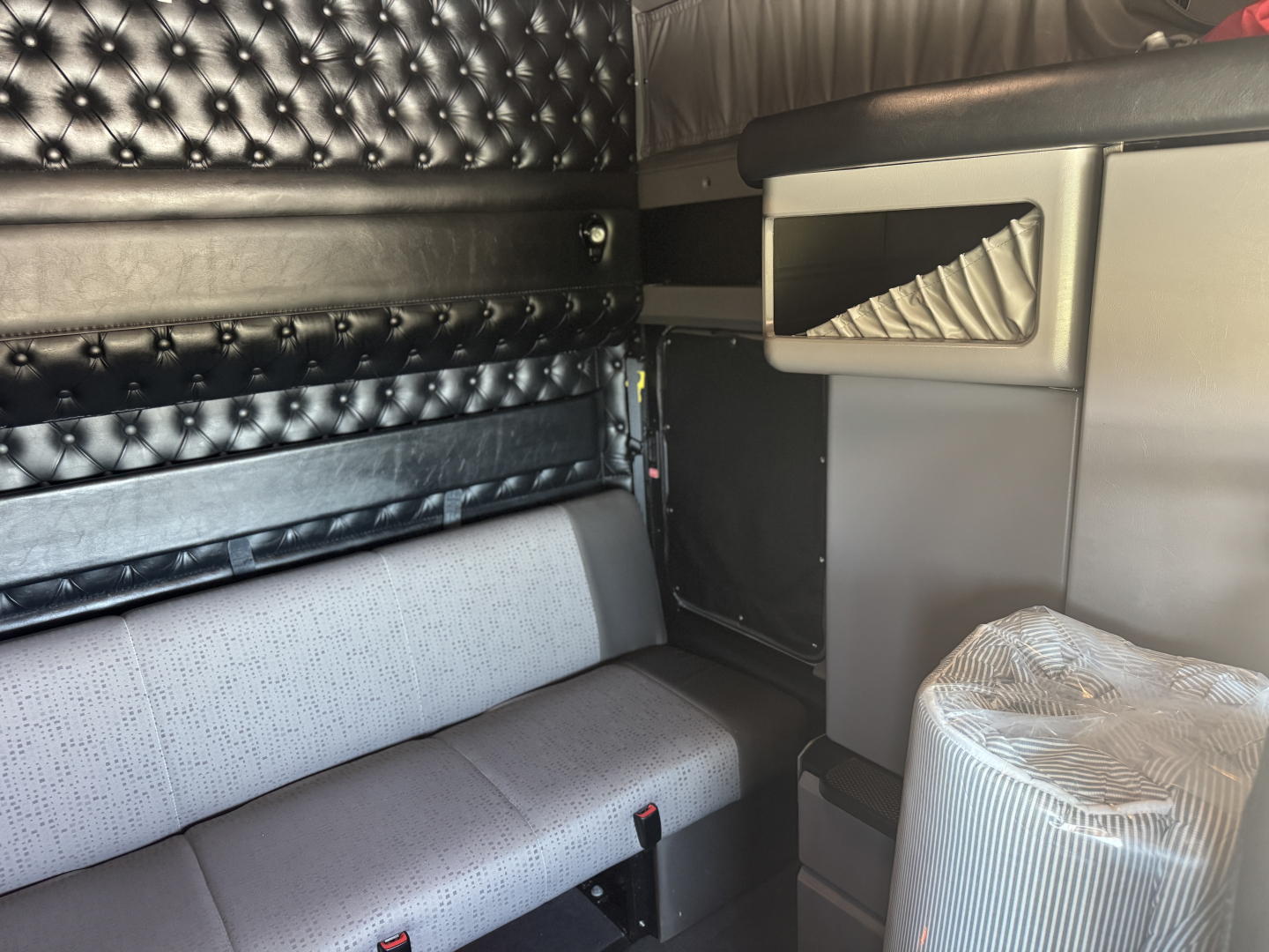 Kenworth W900L tractor cab interior showing black quilted door panel, grey fabric bench seat, and side storage with chrome accents.