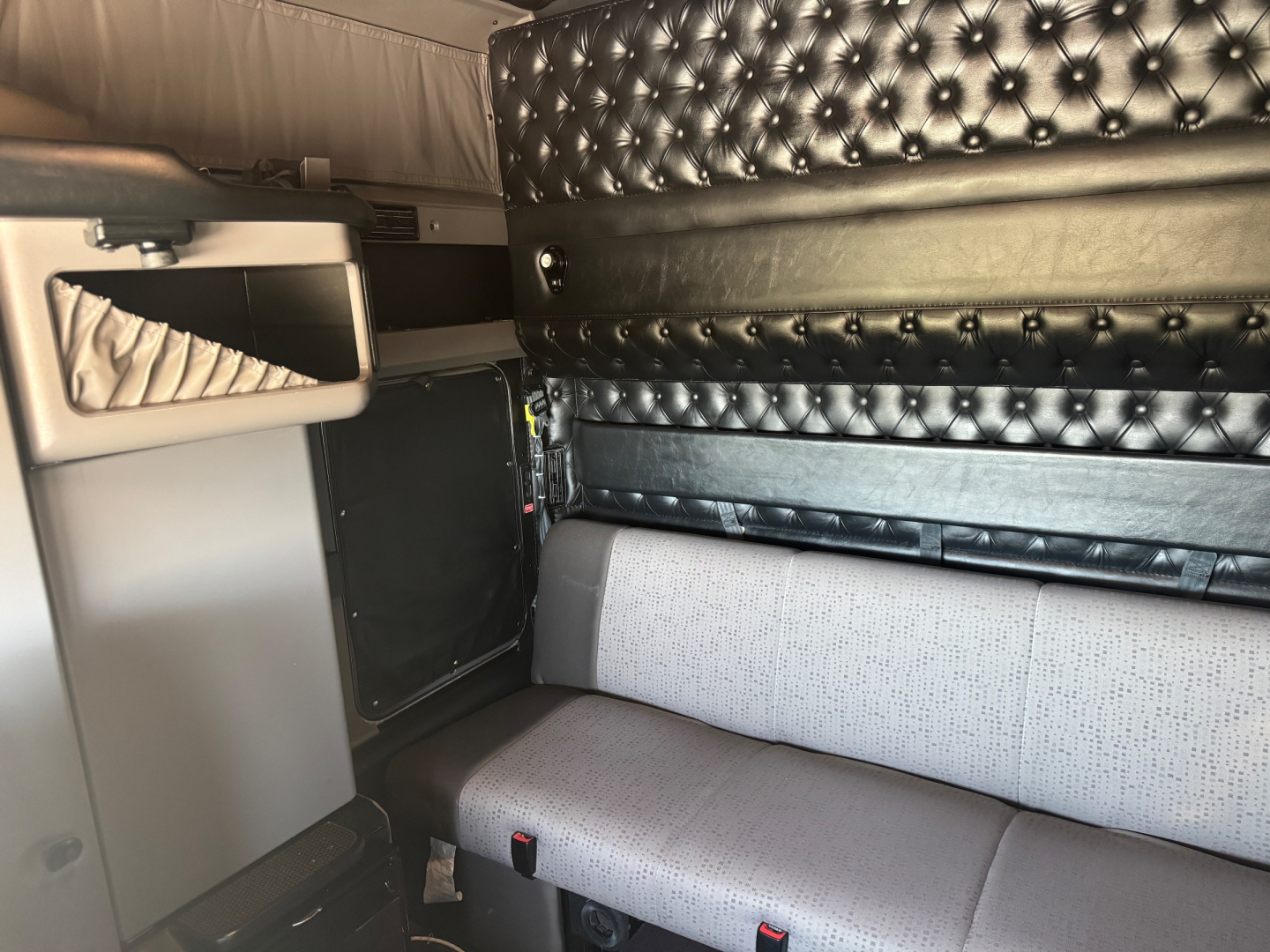 Kenworth W900L truck interior cabin area with black tufted sleeper walls and grey seat, storage cabinet visible.