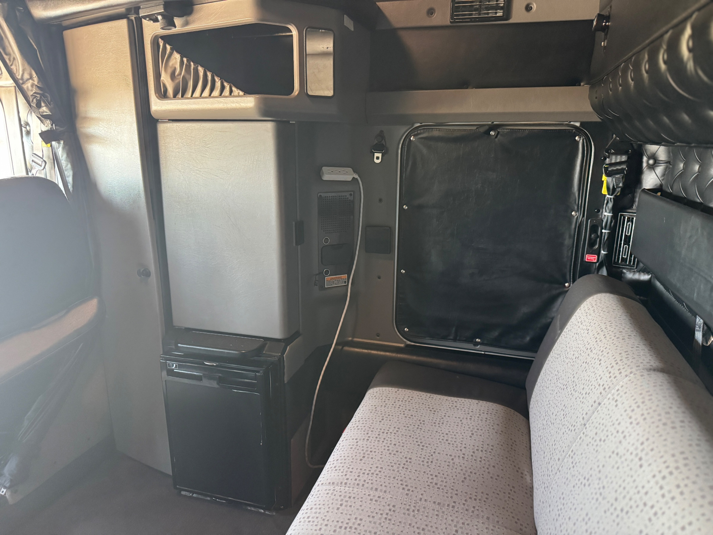 Kenworth W900L sleeper cab interior showing side panel, storage compartment, seating area, and refrigerator unit.
