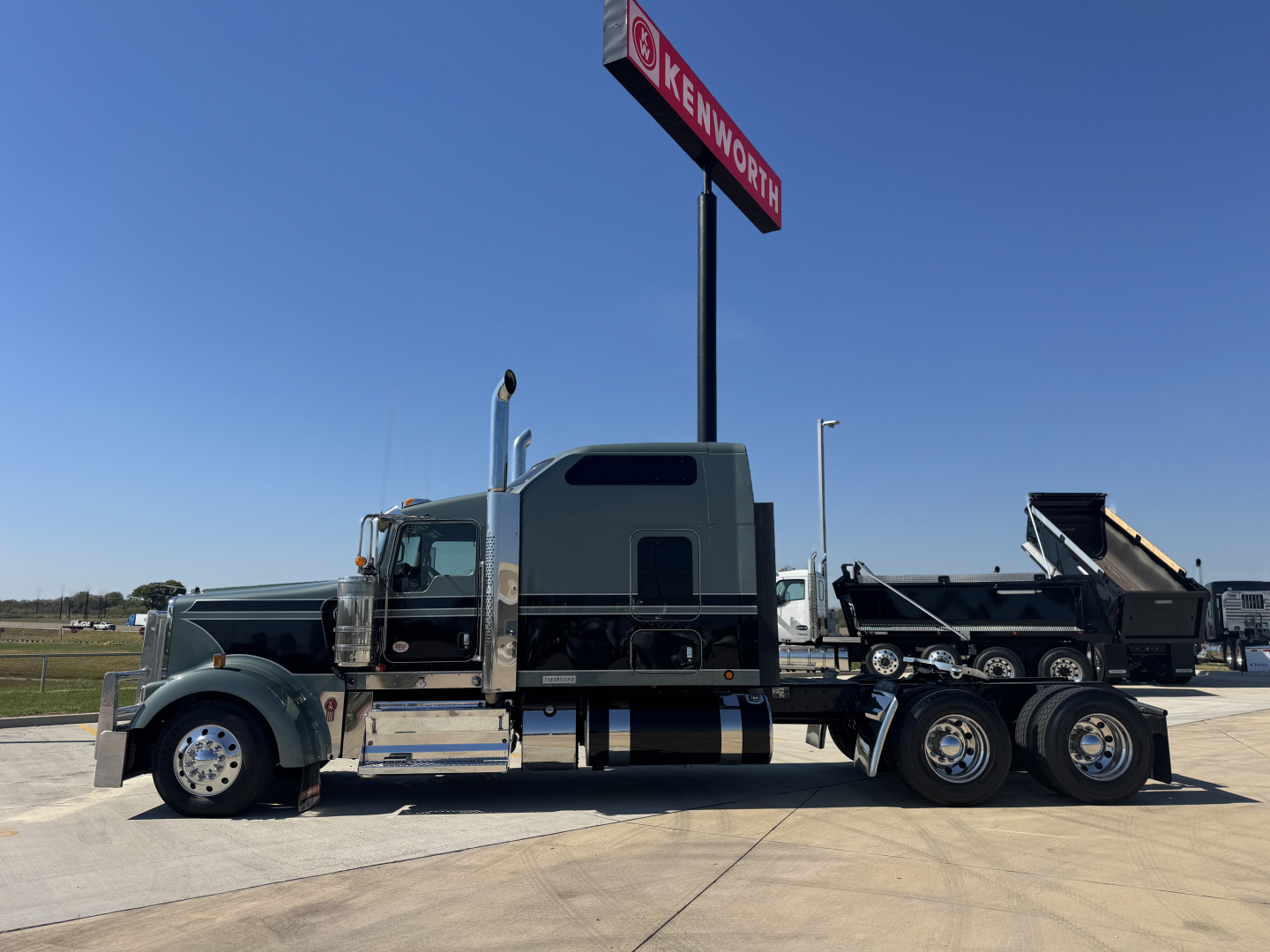 Kenworth W900L conventional sleeper semi-truck with a chrome-detailed cab and a dump trailer attached, side view.