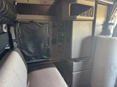 Cab interior of a 2025 Kenworth W900L showing dash controls, storage compartments, and seating; VIN tag and stock number not visible in detail.