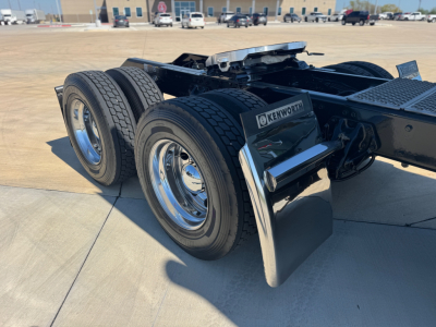 Kenworth W900L chassis rear view showing dual rear axles, mud flaps, chrome wheels, and fuel/air lines.