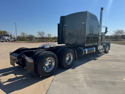 Kenworth W900L sleeper cab tractor (rear/side view) showing dual rear axles, black exterior, chrome fuel tanks, and exhaust stack.