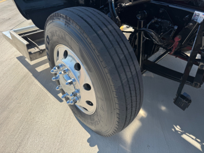 Kenworth W900L front wheel and suspension visible in the engine bay area showing large Tire and wheel assembly.