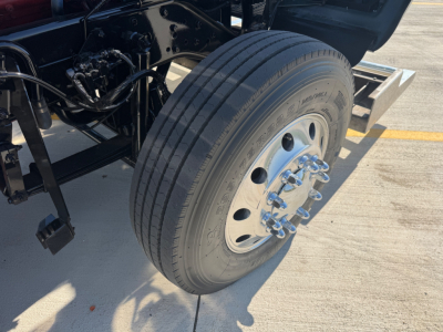 Kenworth W900L front wheel showing dual-wheel hub with lug nuts and large treaded tire in a truck yard.