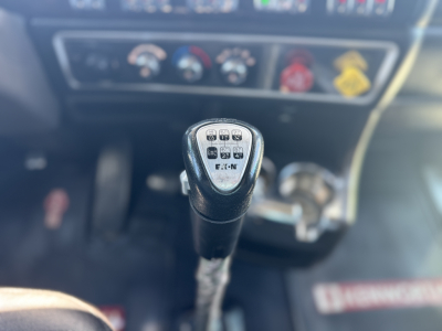 Gear shift knob with shift pattern in a Kenworth W900L interior showing 10-speed Eaton Fuller transmission. Blurred dashboard gauges in background.