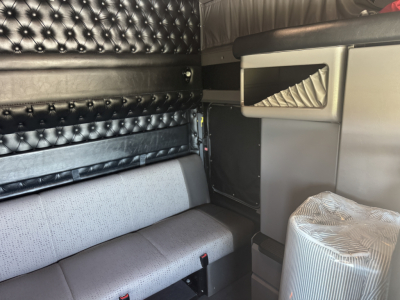 Kenworth W900L tractor cab interior showing black quilted door panel, grey fabric bench seat, and side storage with chrome accents.