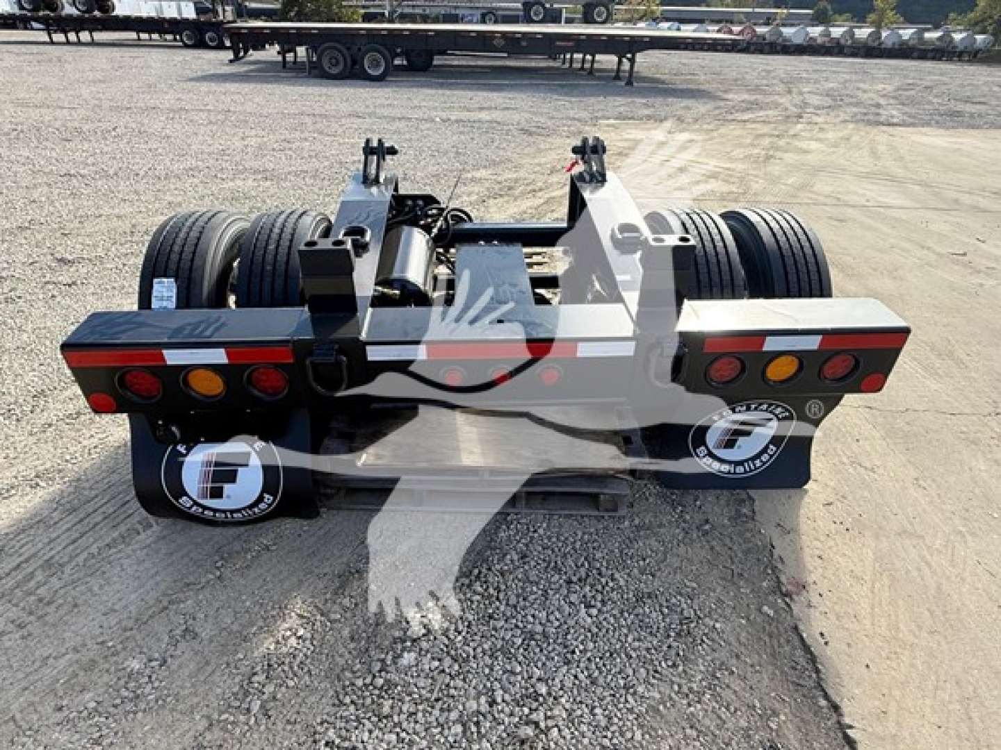 Trailer rear view of a Fontaine flip axle lowboy trailer showing dual rear axles, taillights, and deck structure with VIN label nearby.