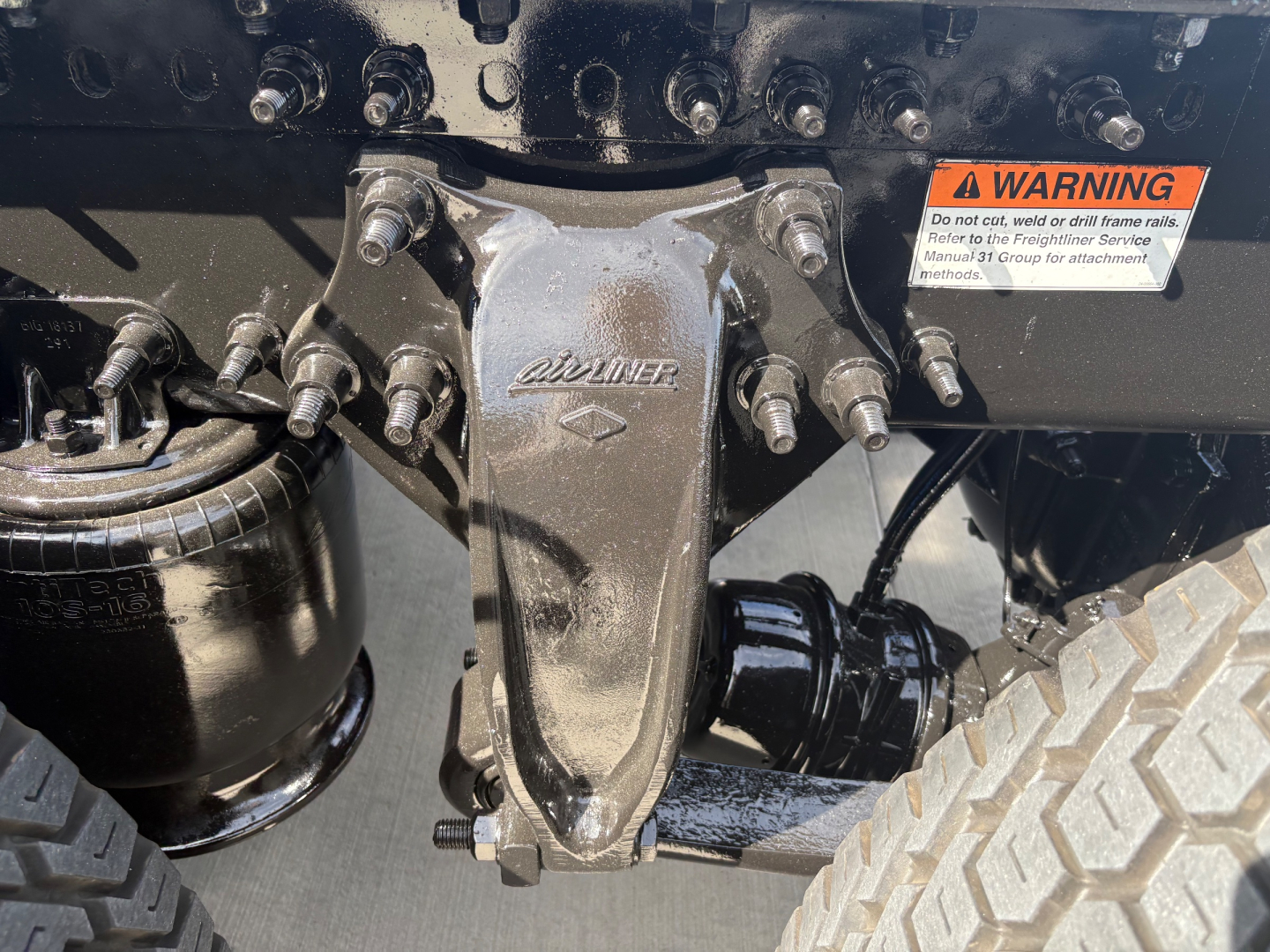 Vehicle rear view showing drivetrain torque linkage with ‘Avery’/AXLE component, warning label, and heavy-duty hitch in a Freightliner PT126064ST truck.