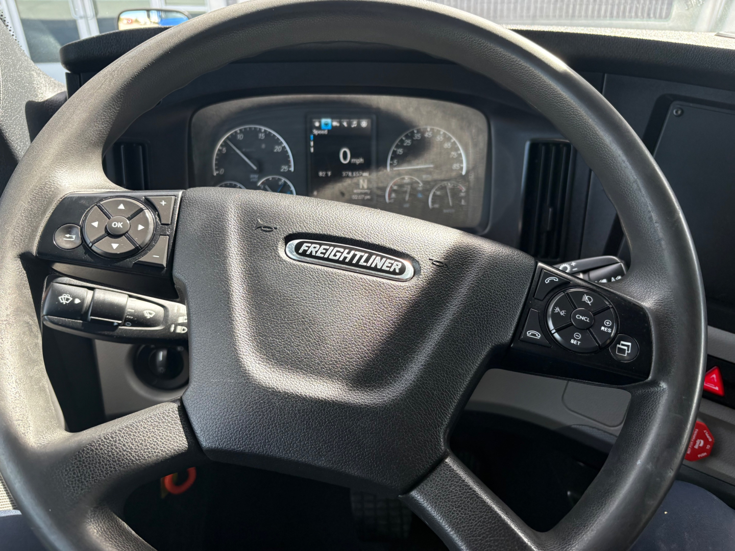 Freightliner steering wheel with logo visible and instrument cluster in background inside a sleeper truck cab.