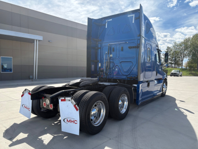 Blue Freightliner semi-truck tractor cab rear view showing dual rear axles and fifth wheel, with mud flaps labeled MHC.