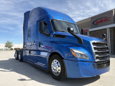 Truck cab with blue Freightliner semi-truck showing front grille and side mirror.