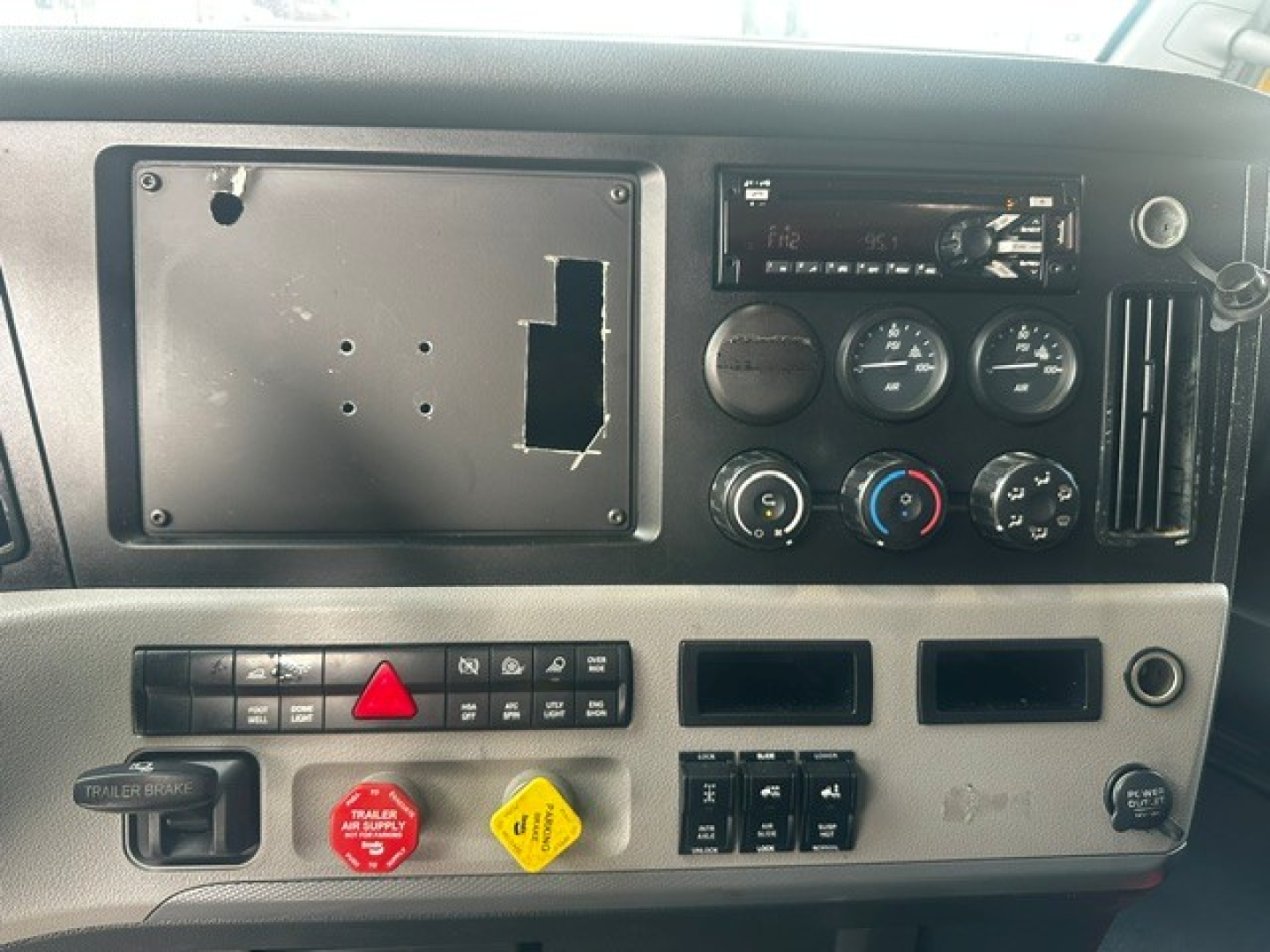 Dashboard panel of a 2019 Freightliner Cascadia 126 showngeometer gauges, control switches, and radio; blank mount plate on left where a display may be installed.