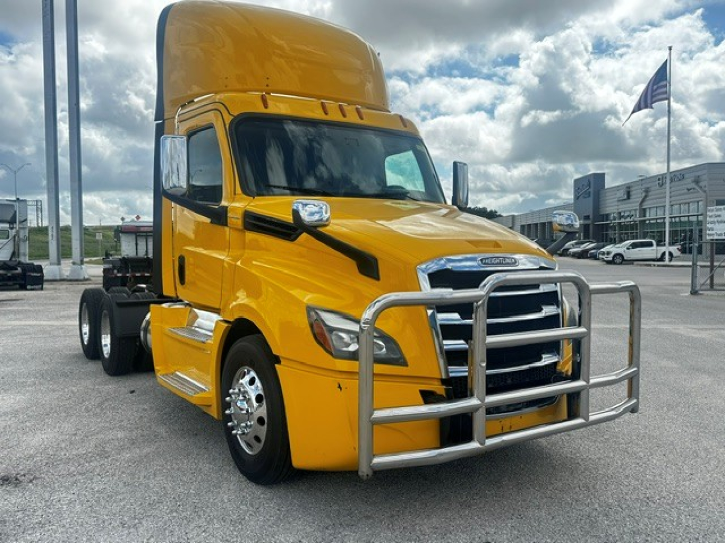 Yellow Freightliner Cascadia 126 daycab truck in a dealership lot, chrome grille guard, large sleeper cabin, front left view with badge and headlights visible.